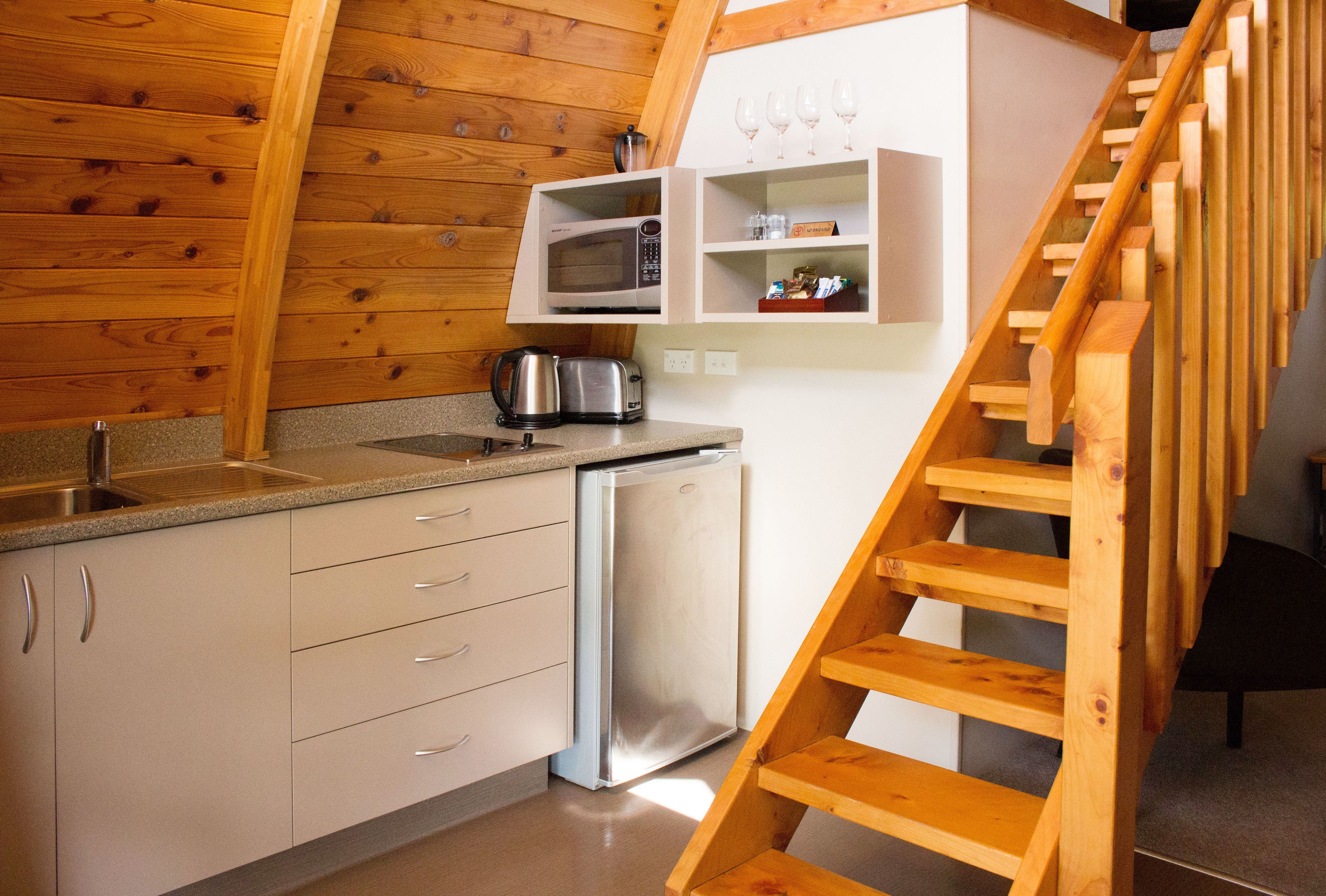A kitchen with wooden walls, a stainless steel refrigerator, a microwave, and a kettle.