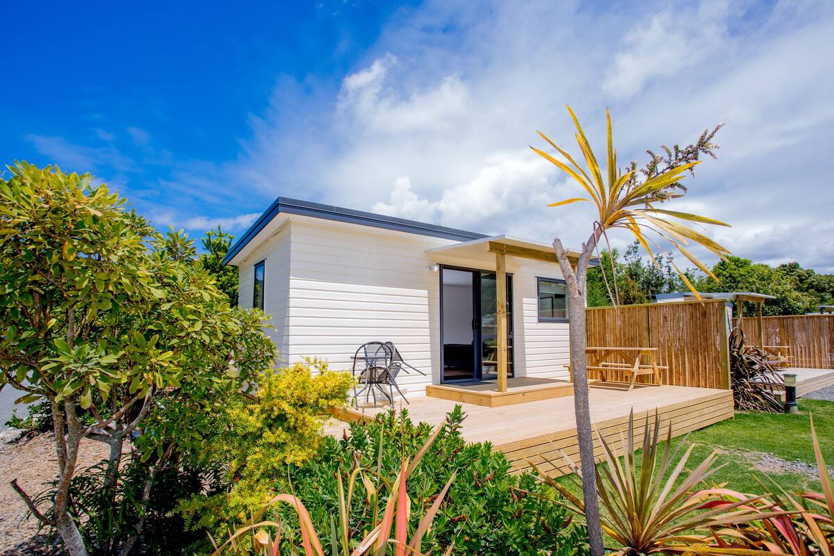 Una casa moderna con terraza de madera, puerta de cristal y patio con mobiliario exterior.
