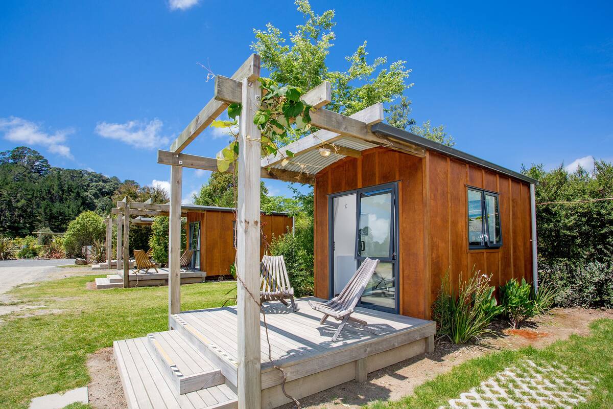 Una cabaña de madera con terraza, dos sillones de descanso y una pérgola.