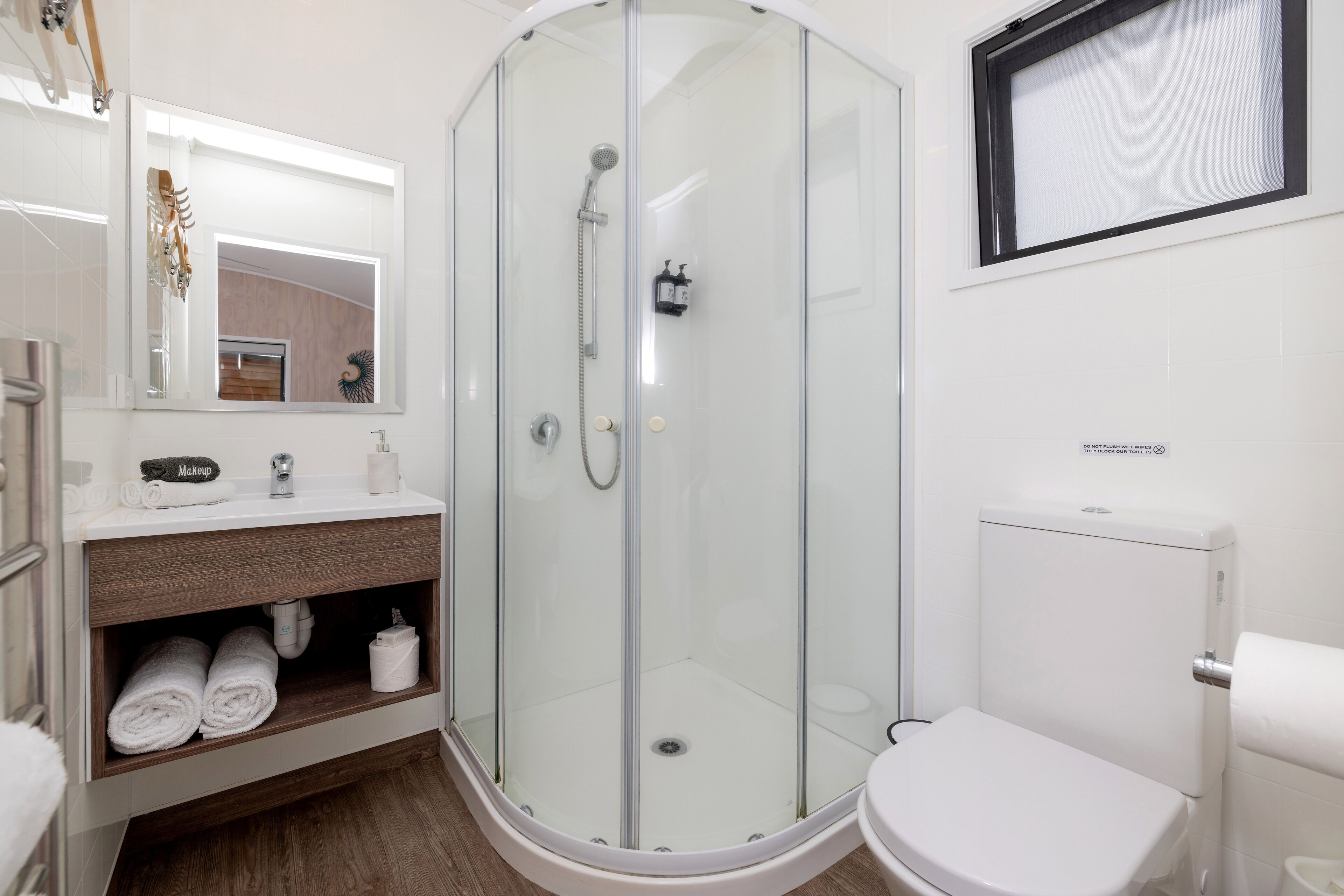 A modern bathroom with a glass-enclosed shower, a white toilet, and a vanity with towels.