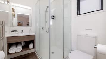 A modern bathroom with a glass-enclosed shower, a white toilet, and a vanity with towels.