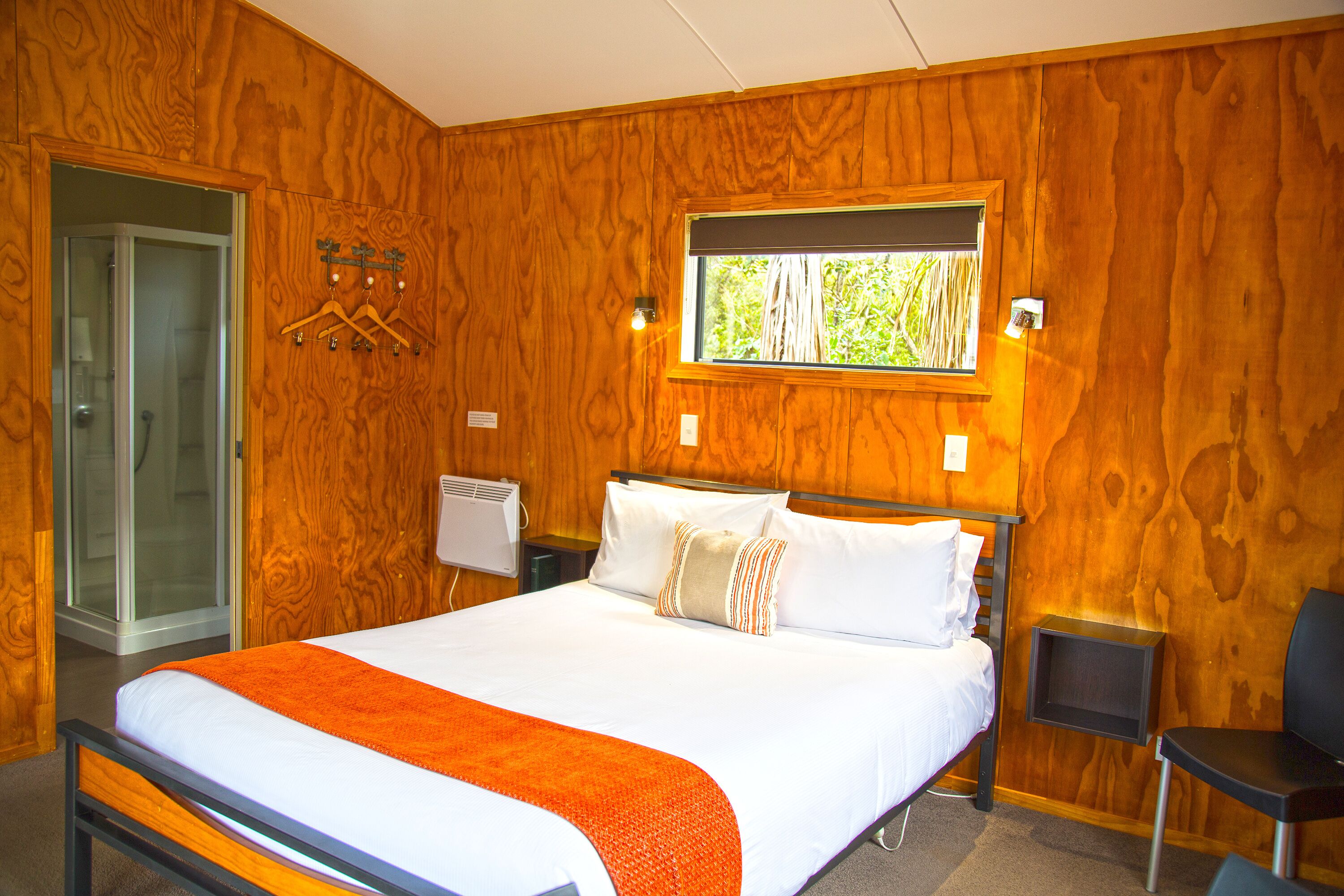 A wooden-paneled room with a bed, a window, a desk, and a chair.