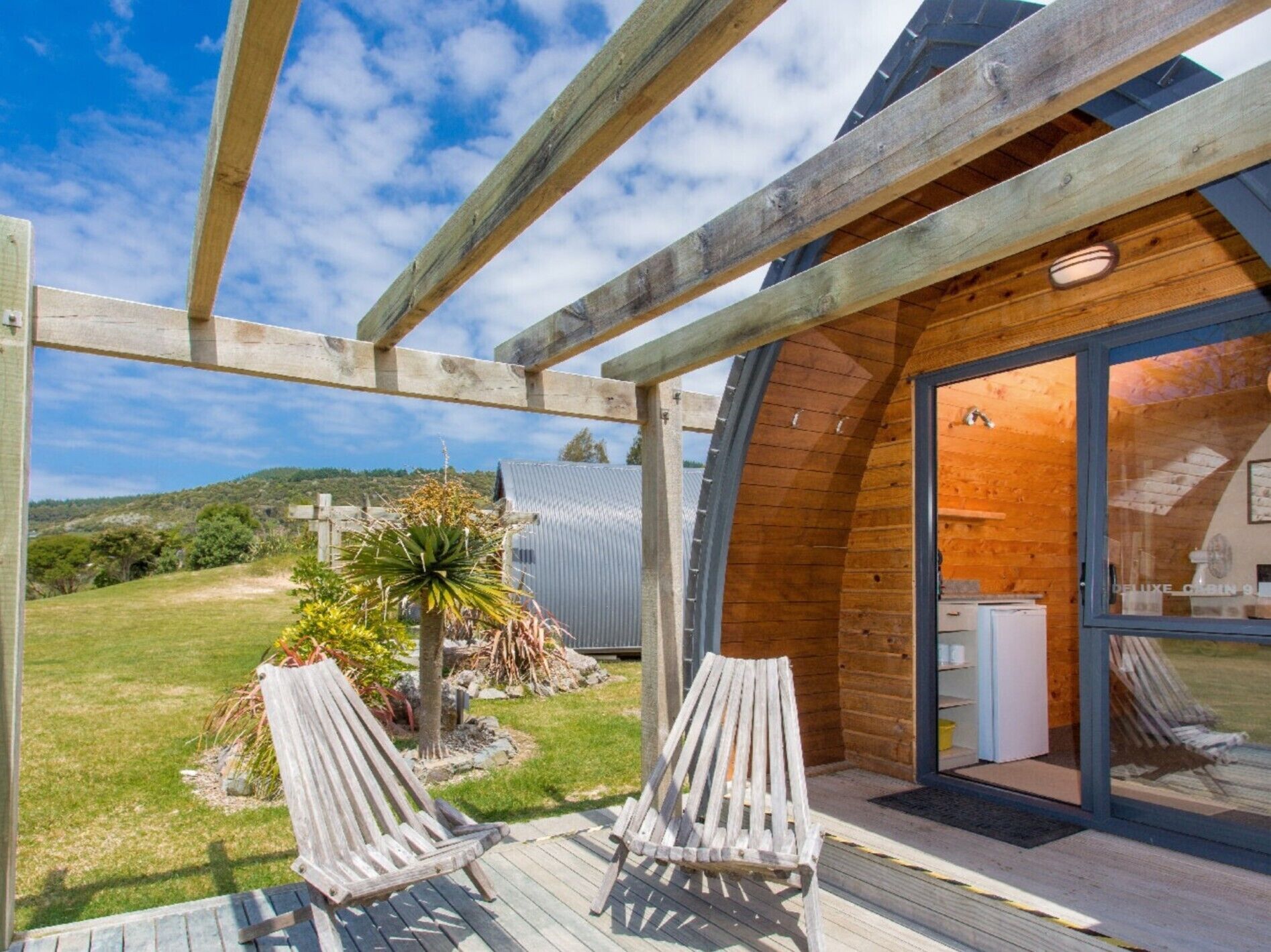 A wooden cabin with a glass door leading to a deck with two chairs.