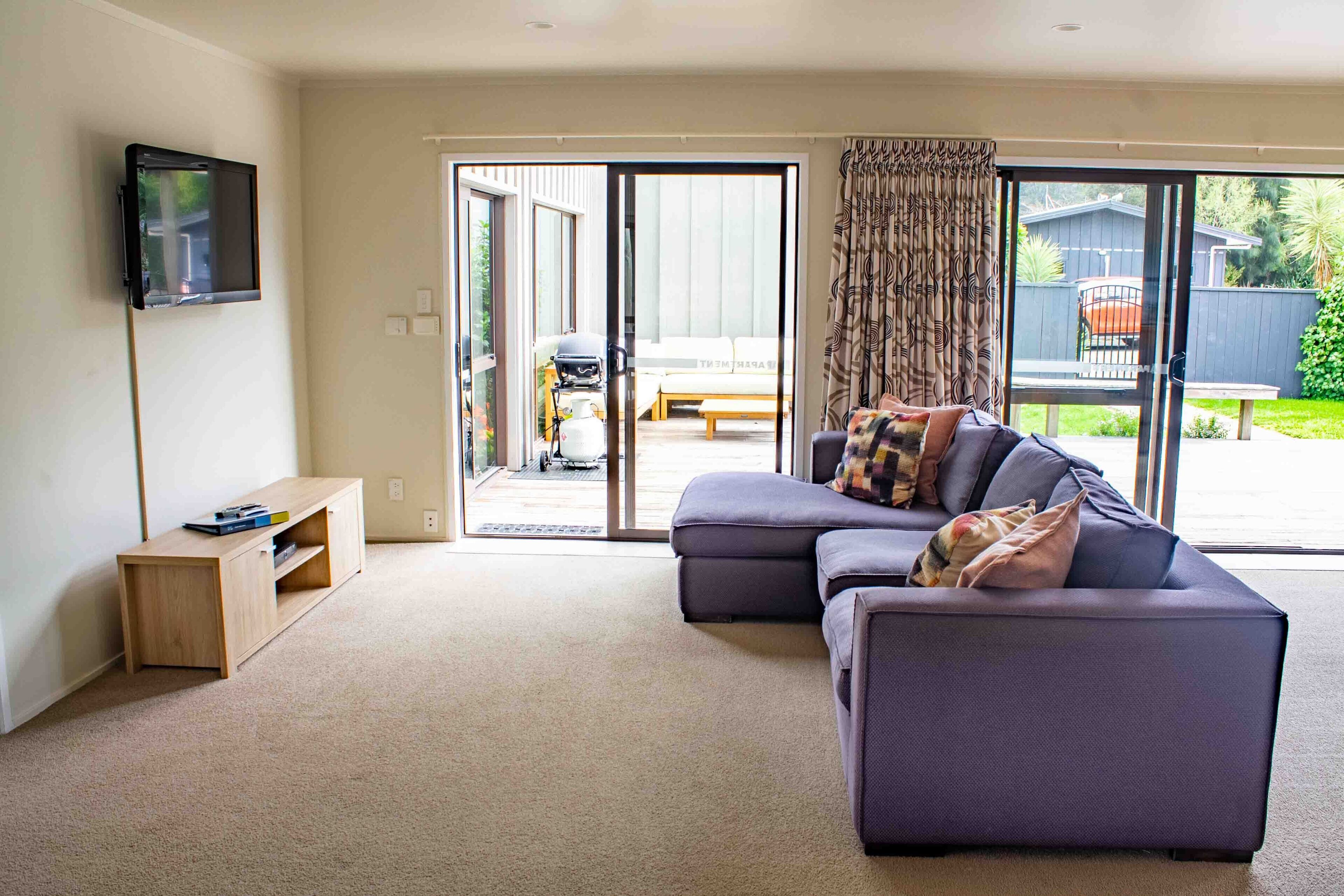 A modern living room with a sofa, a flat-screen TV, and a sliding glass door leading to an outdoor patio.