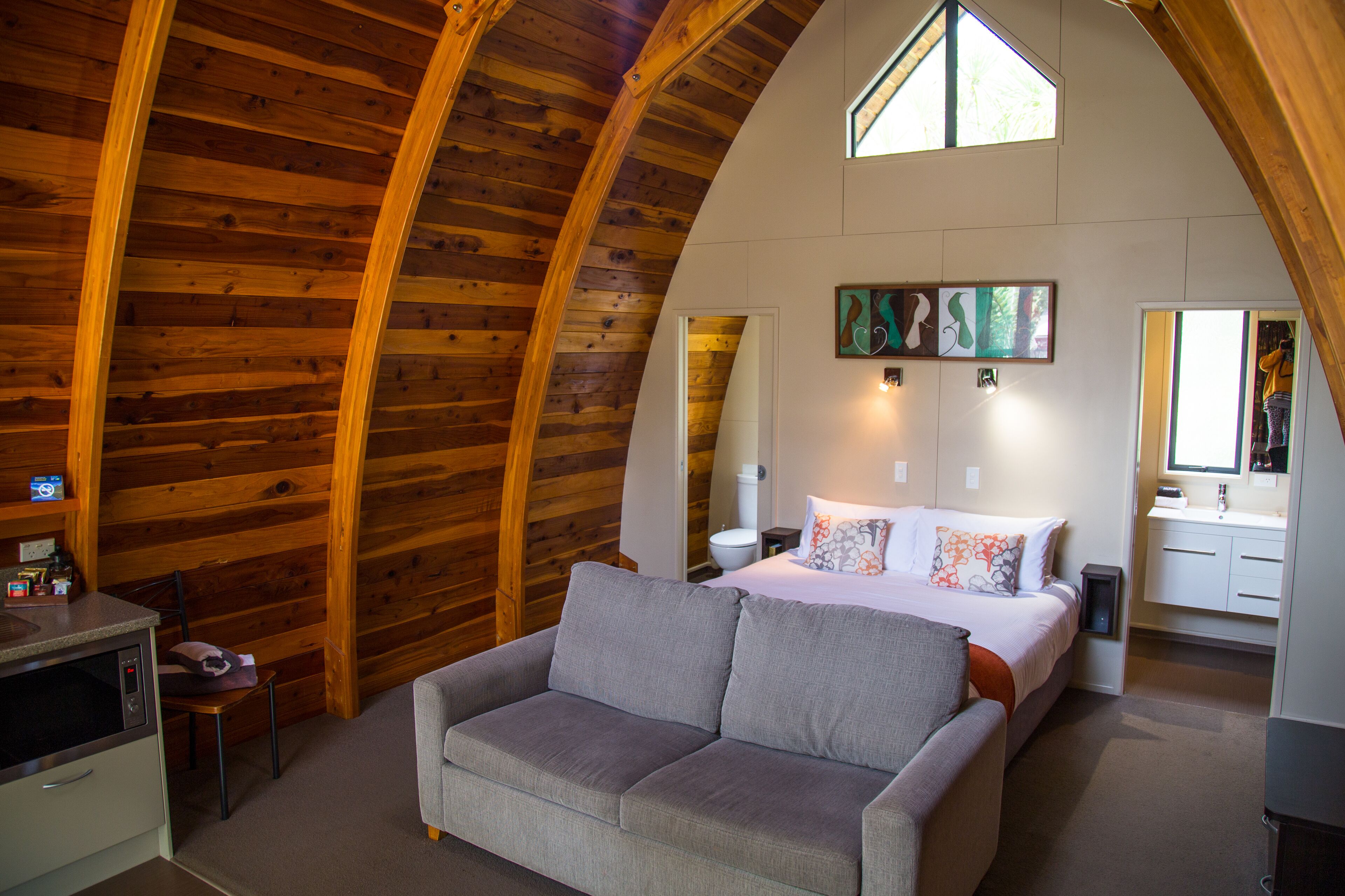 Een knus ogende kamer met houten plafond, een bed met kussens, een bank, een kleine tafel en een spiegel.