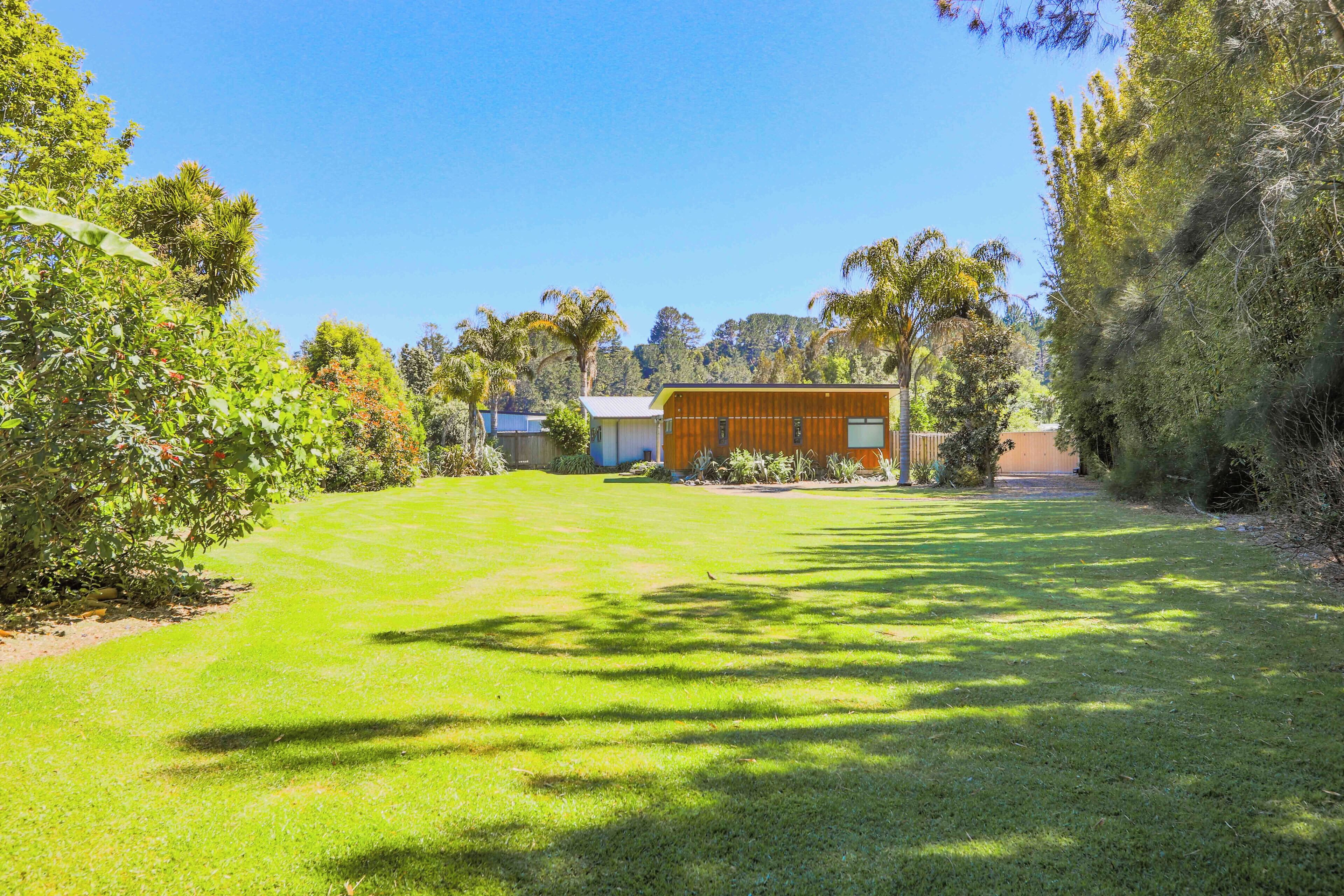 A modern house with a well-maintained lawn, surrounded by dense vegetation and trees.