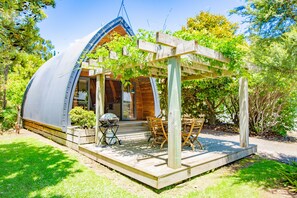 Una casa con forma de cúpula, con terraza de madera, mobiliario exterior y una parrilla.