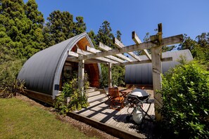 Una estructura moderna, semiabierta, con techo curvo, terraza de madera y zona de estar al aire libre.