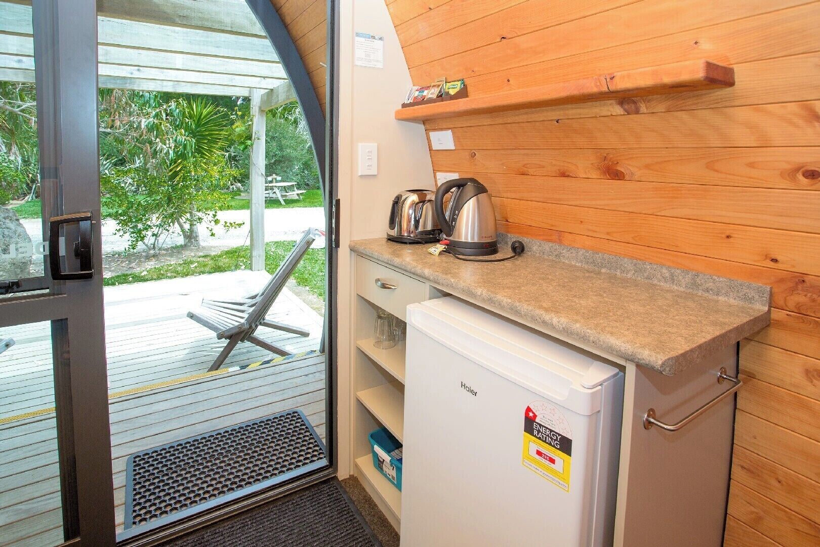 A compact kitchenette with a small refrigerator, a coffee maker, and a kettle on the countertop.