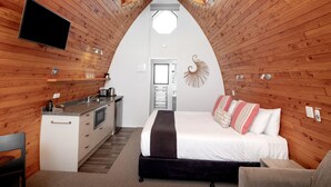 Une pièce chaleureuse aux murs lambrissés, avec un lit, un bureau et un téléviseur.