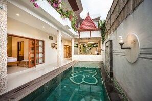 A modern indoor pool area with a clear water feature, a wooden deck, and a small bridge. - Maha Residence Guest House (Jimbaran)
