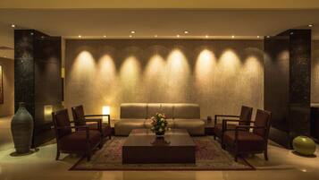 Un lobby moderno con un sofá, sillas, una mesita de centro y una pared texturizada con iluminación.