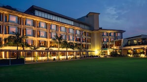 Um hotel de vários andares com uma grande fachada de vidro, área de estar ao ar livre e um gramado bem cuidado.