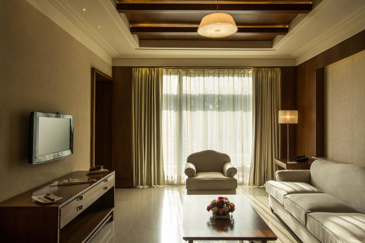 A modern living room with a flat-screen TV, a sofa, a coffee table with flowers, and a large window with curtains.
