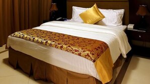 A hotel room with a large bed, a headboard, two bedside tables, and a nightstand. - Paragon Hotel Apartments (Abu Dhabi)