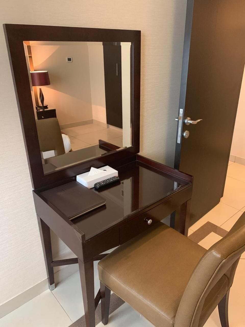 A hotel room with a desk, chair, and a mirror.