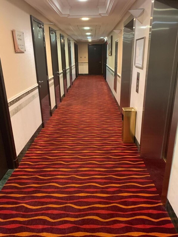 A hotel hallway with a red carpet, multiple doors, and a trash bin.