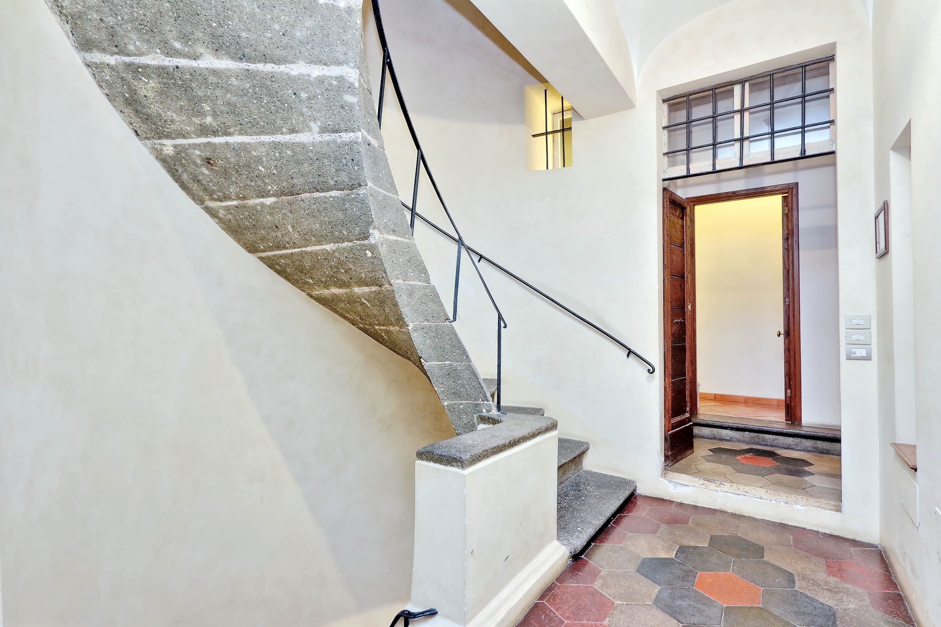 A staircase with stone steps and a handrail, leading to a door with a geometric-patterned floor.
