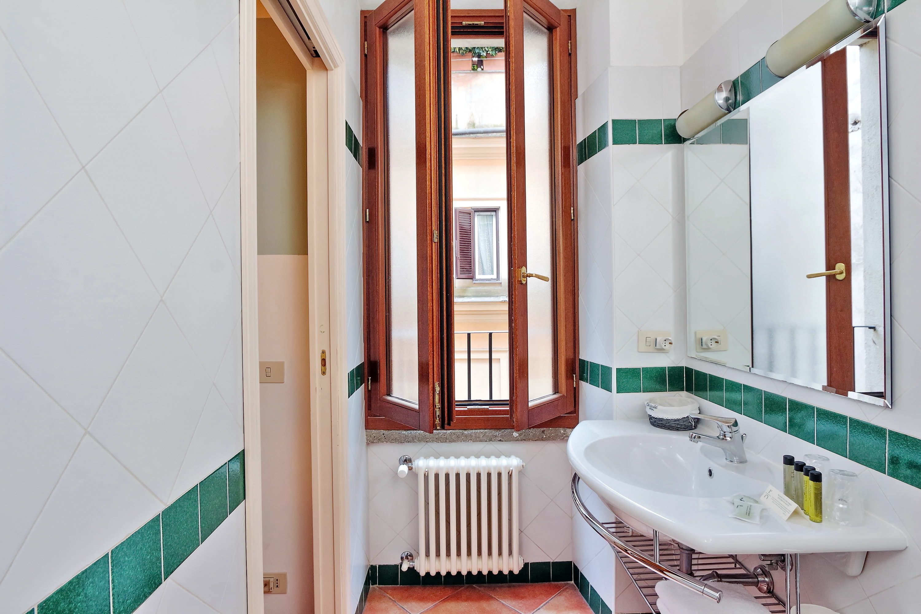 A bathroom with a white sink, a mirror, and a window with wooden shutters.