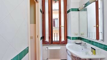A bathroom with a white sink, a mirror, and a window with wooden shutters.