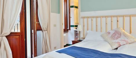 A neatly made bed with white and blue bedding, a wooden headboard, and a window with curtains.