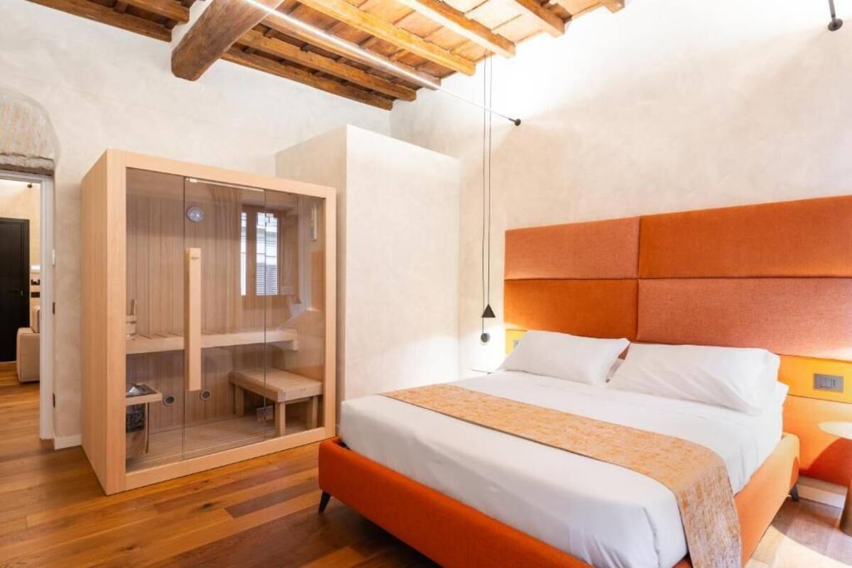 A modern bedroom with a wooden ceiling, a large bed with an orange headboard, and a glass-fronted wardrobe.
