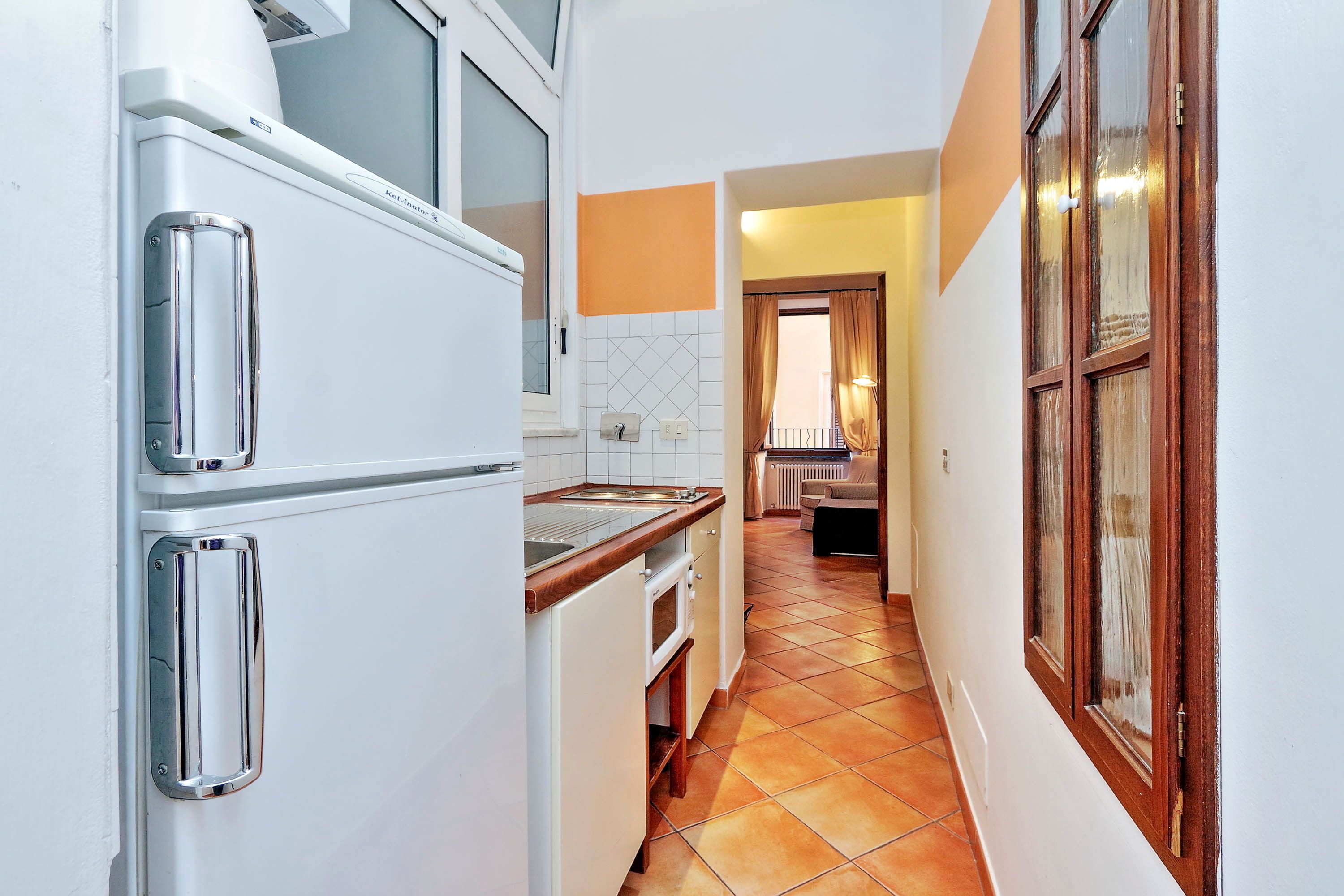Um corredor estreito com uma área de cozinha à esquerda, com uma geladeira e forno brancos.