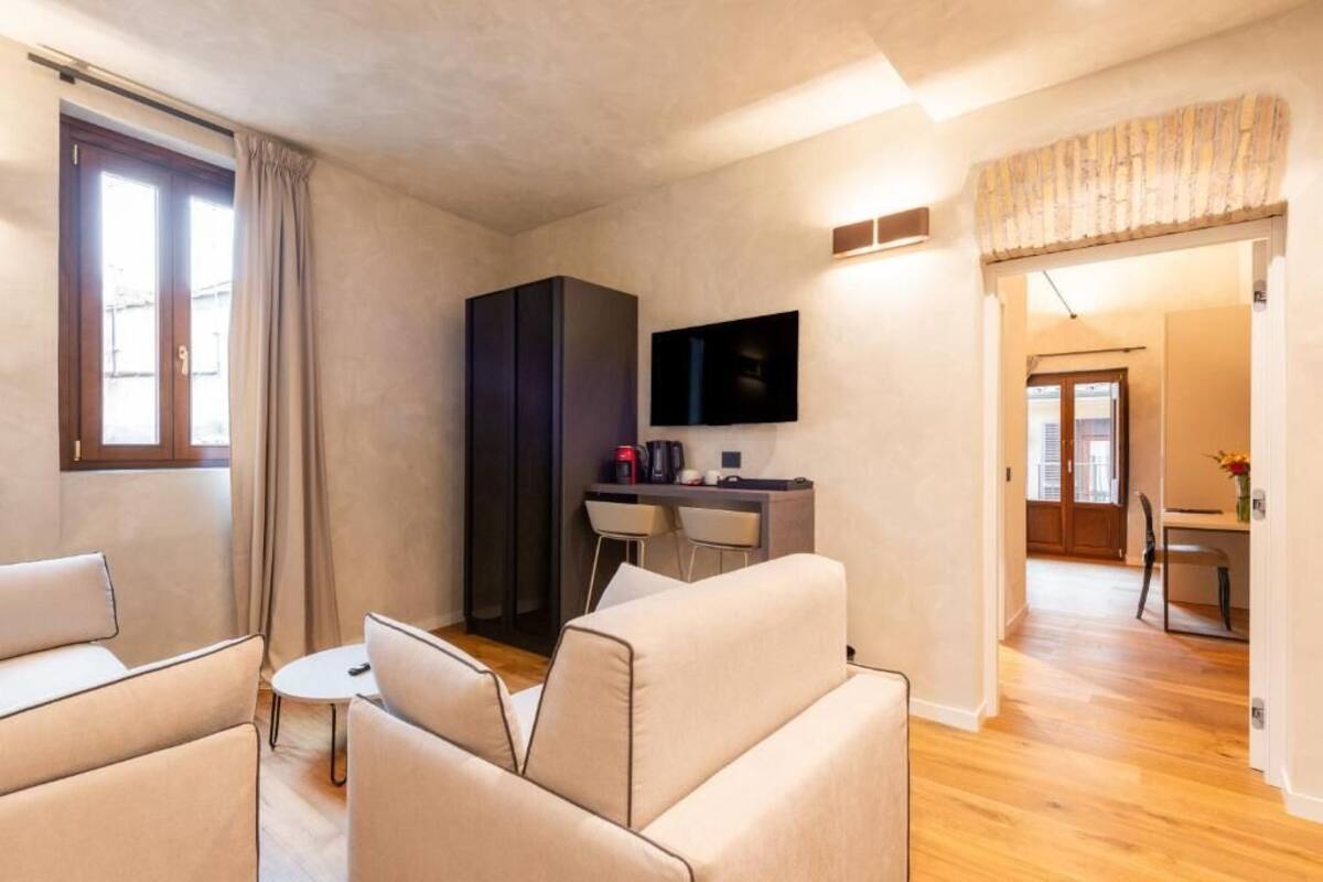 A modern living room with a sofa, a small round table, a TV mounted on the wall, and a kitchenette area with a counter and chairs.