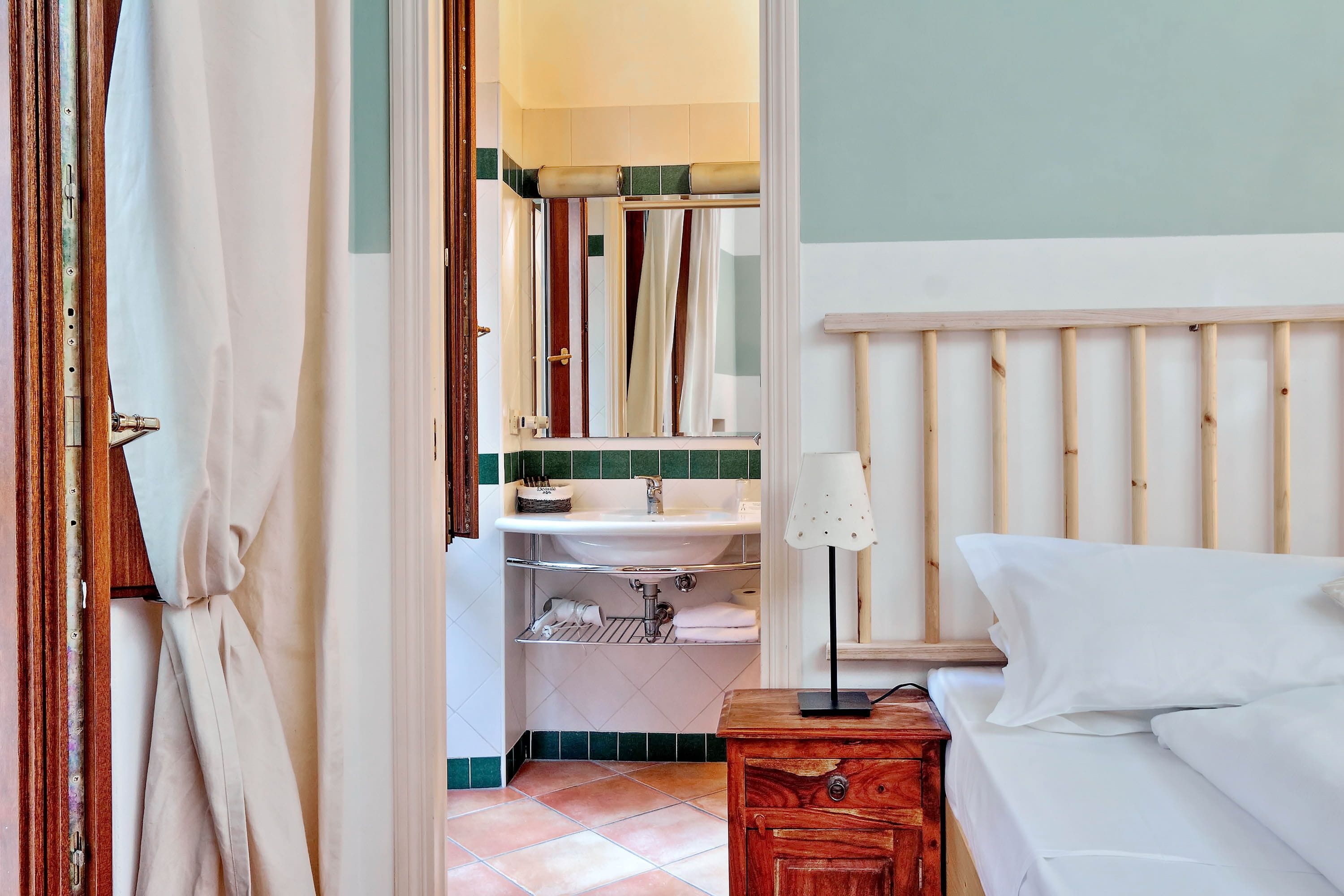 Un dormitorio con cabecera de madera, una mesita de noche con lámpara y una cama blanca.