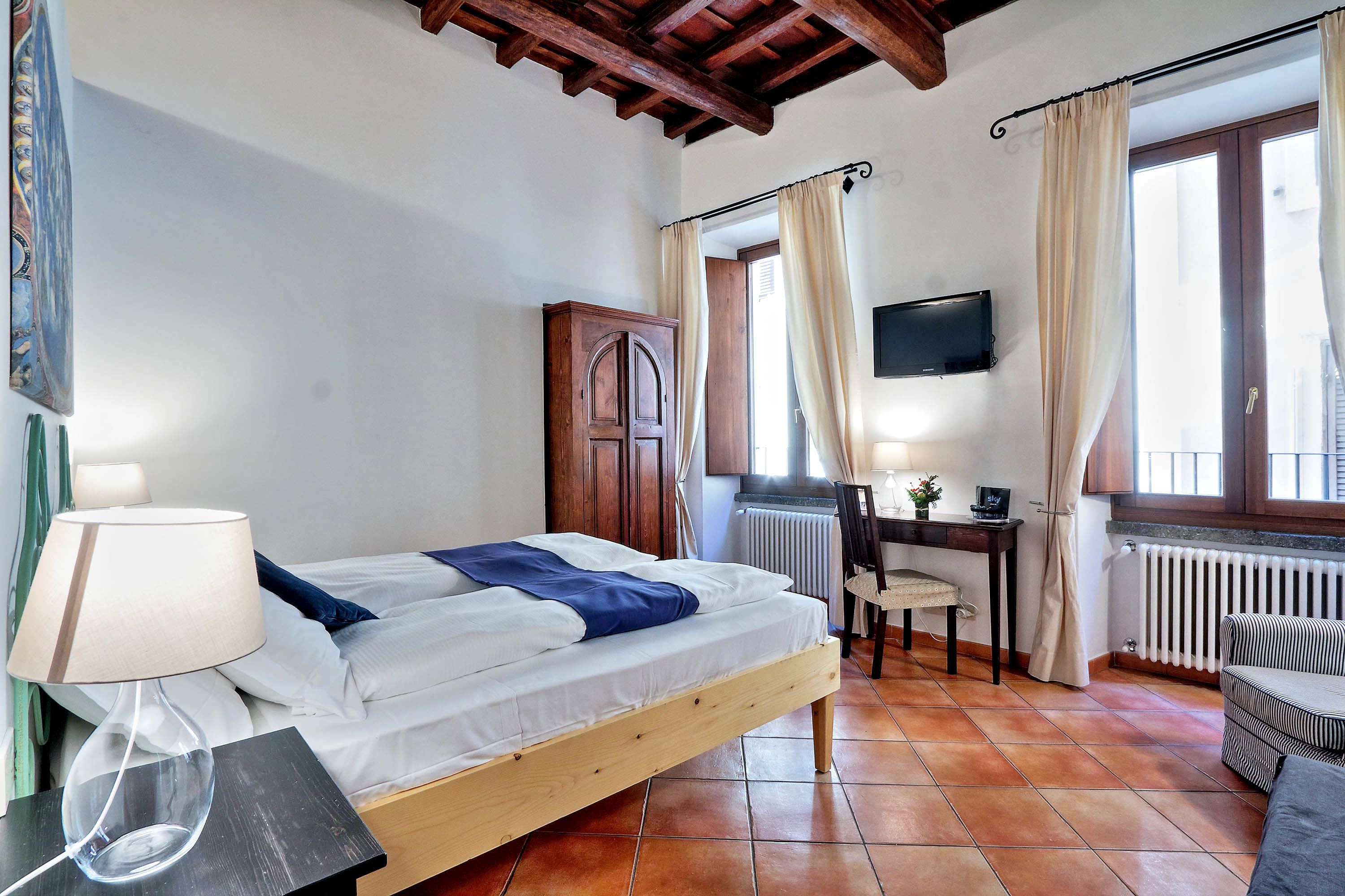 A bedroom with a bed, a desk, a chair, a TV, and a radiator.