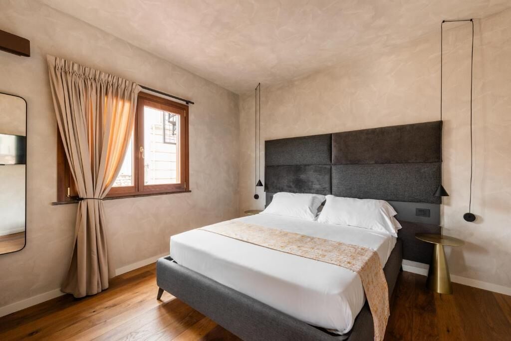 A bedroom with a bed, curtains, a bedside table, and a wall-mounted lamp.