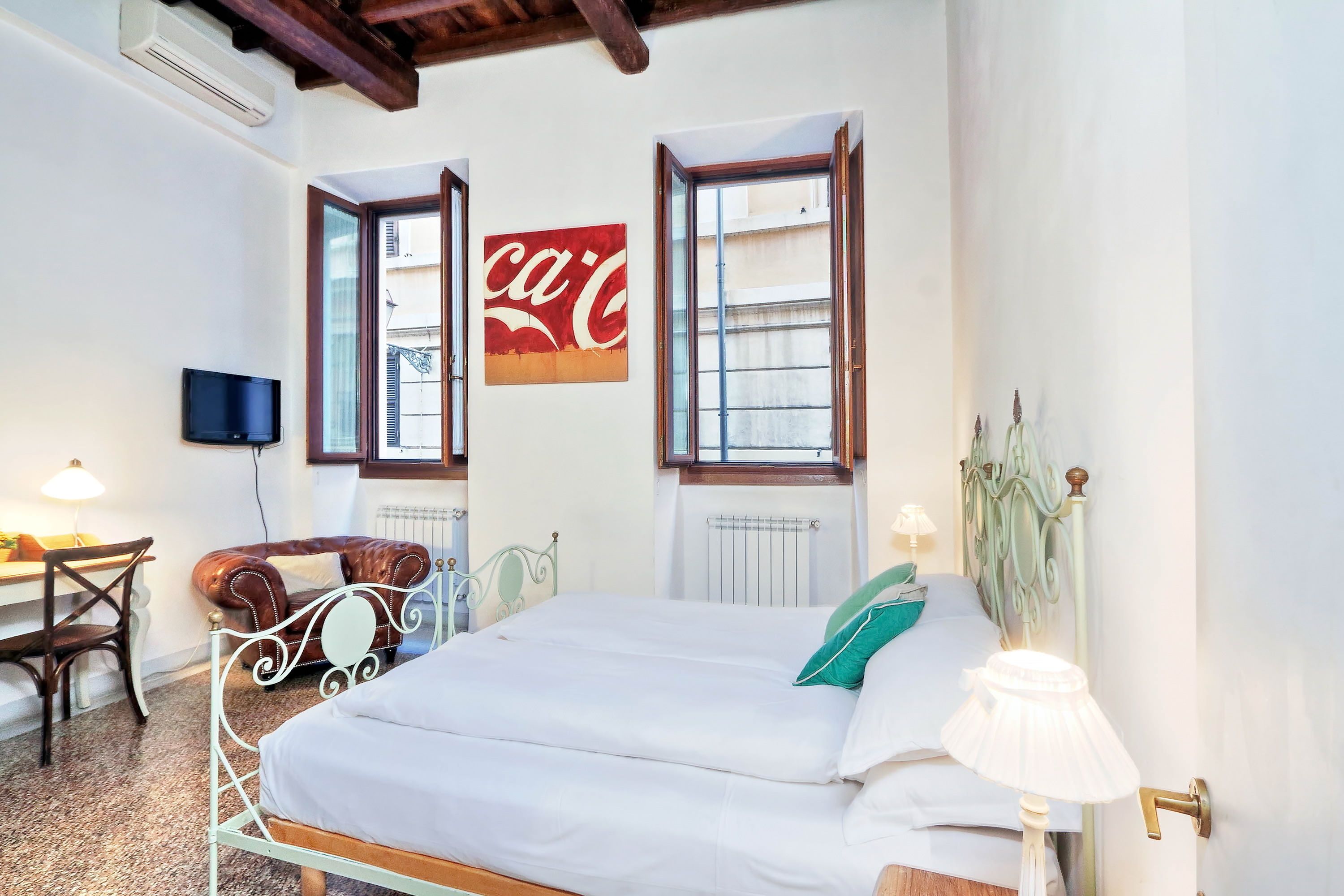 Una camera da letto con un letto, una scrivania, una sedia, una televisione e due finestre con tende.