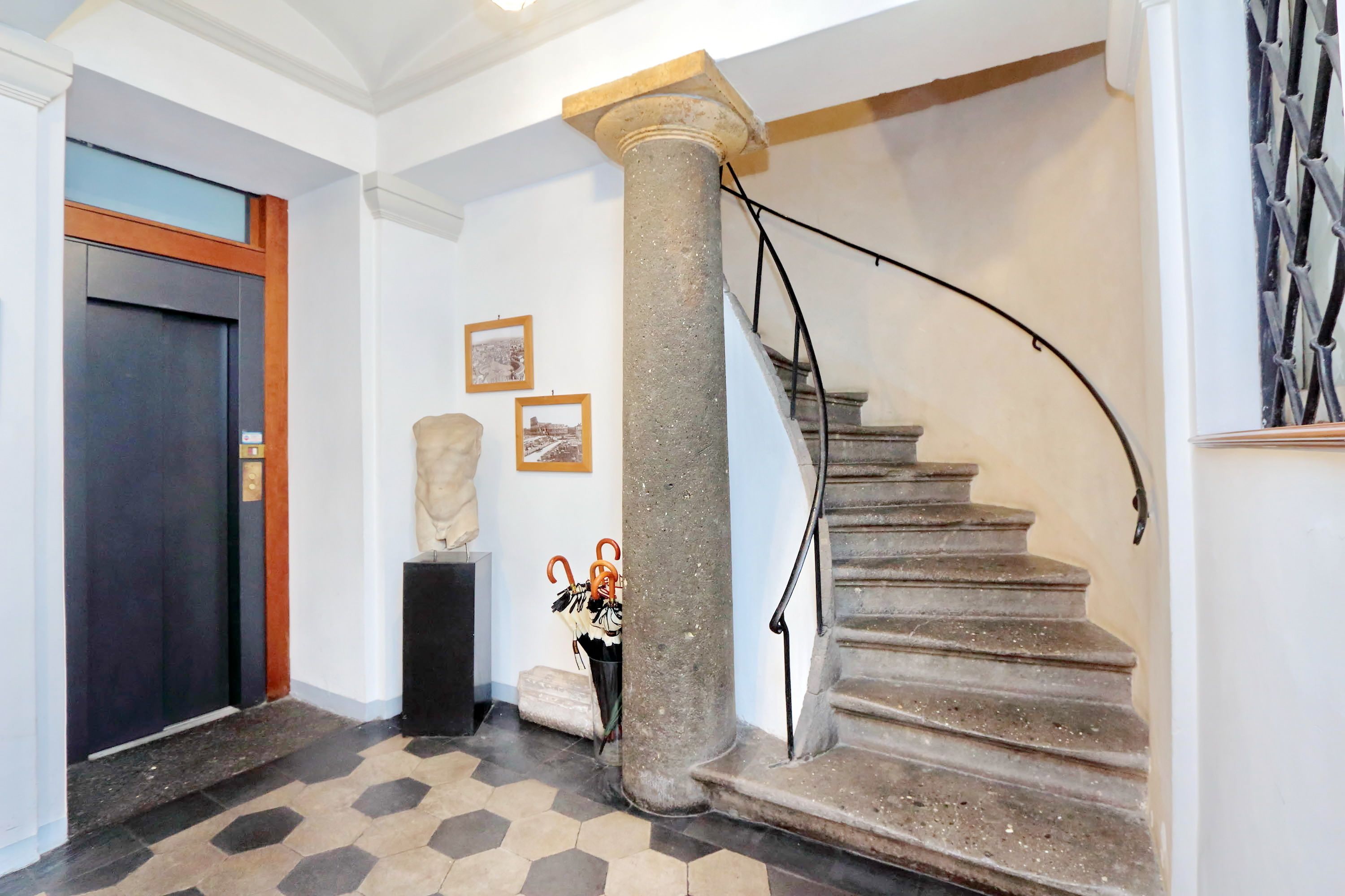 A staircase with a stone column, a dark door, and a tiled floor.