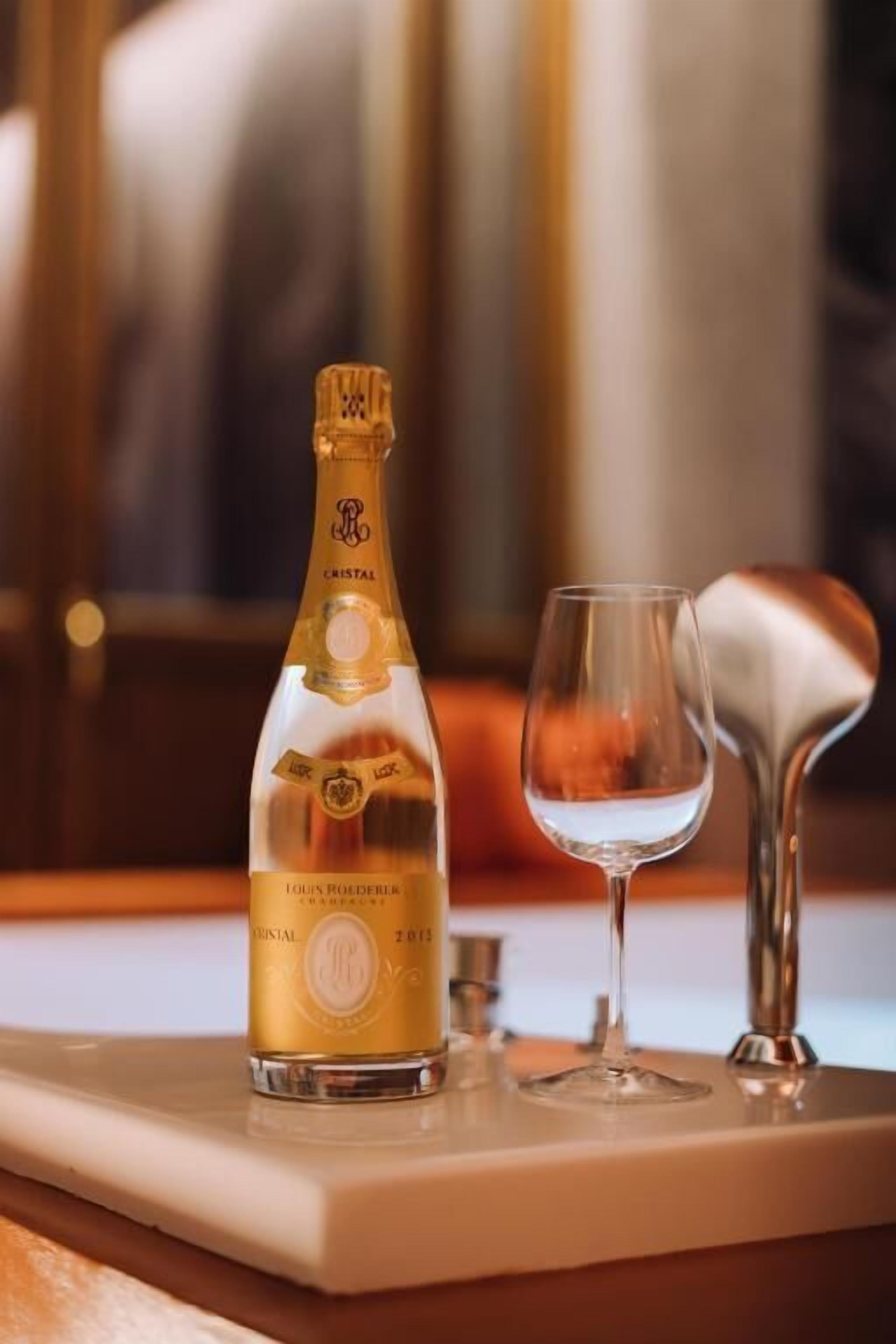 Uma garrafa de champanhe Cristal e uma taça em um tabuleiro.
