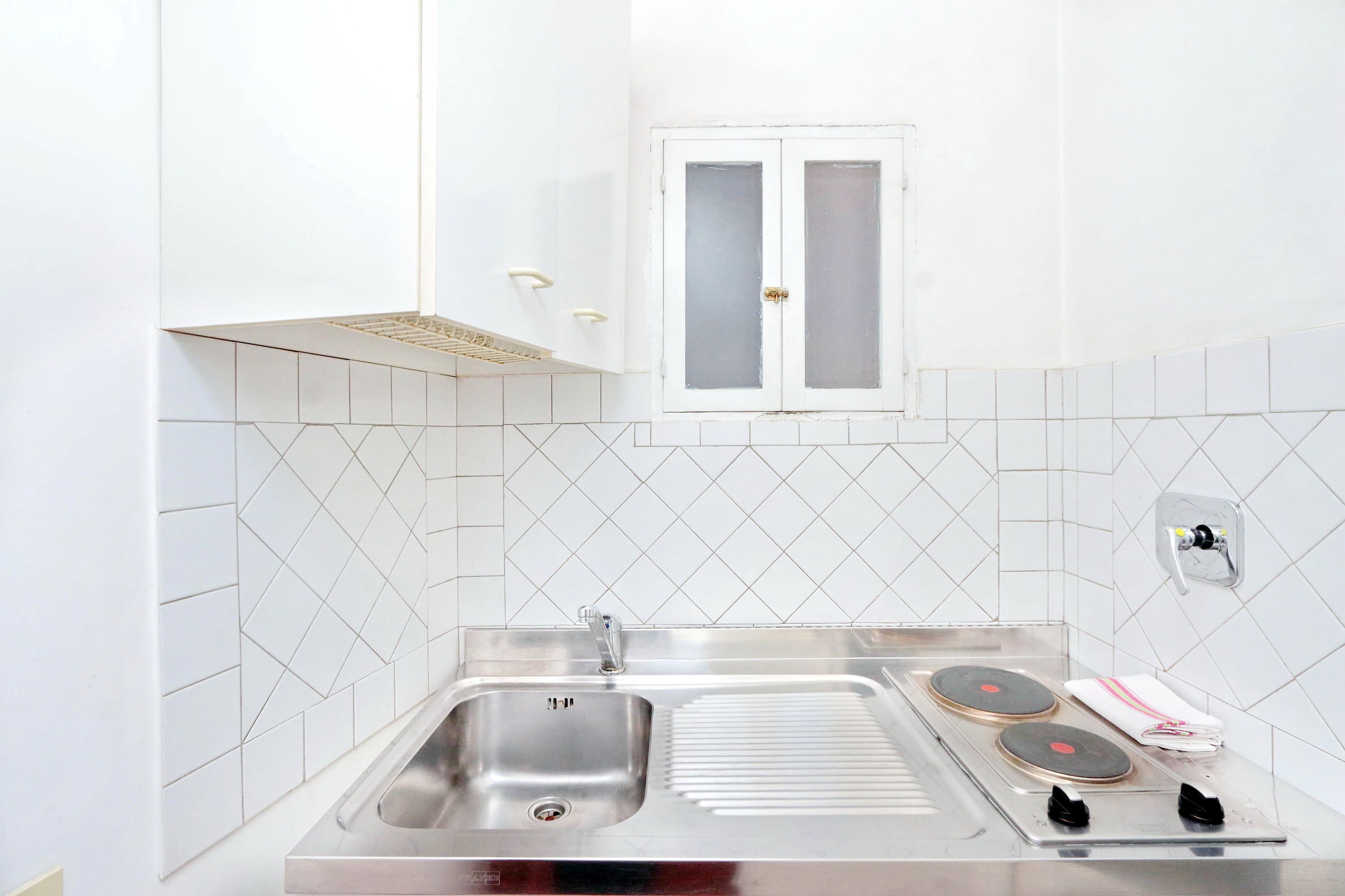 A kitchen with a stainless steel sink, two electric stoves, and a window with frosted glass.