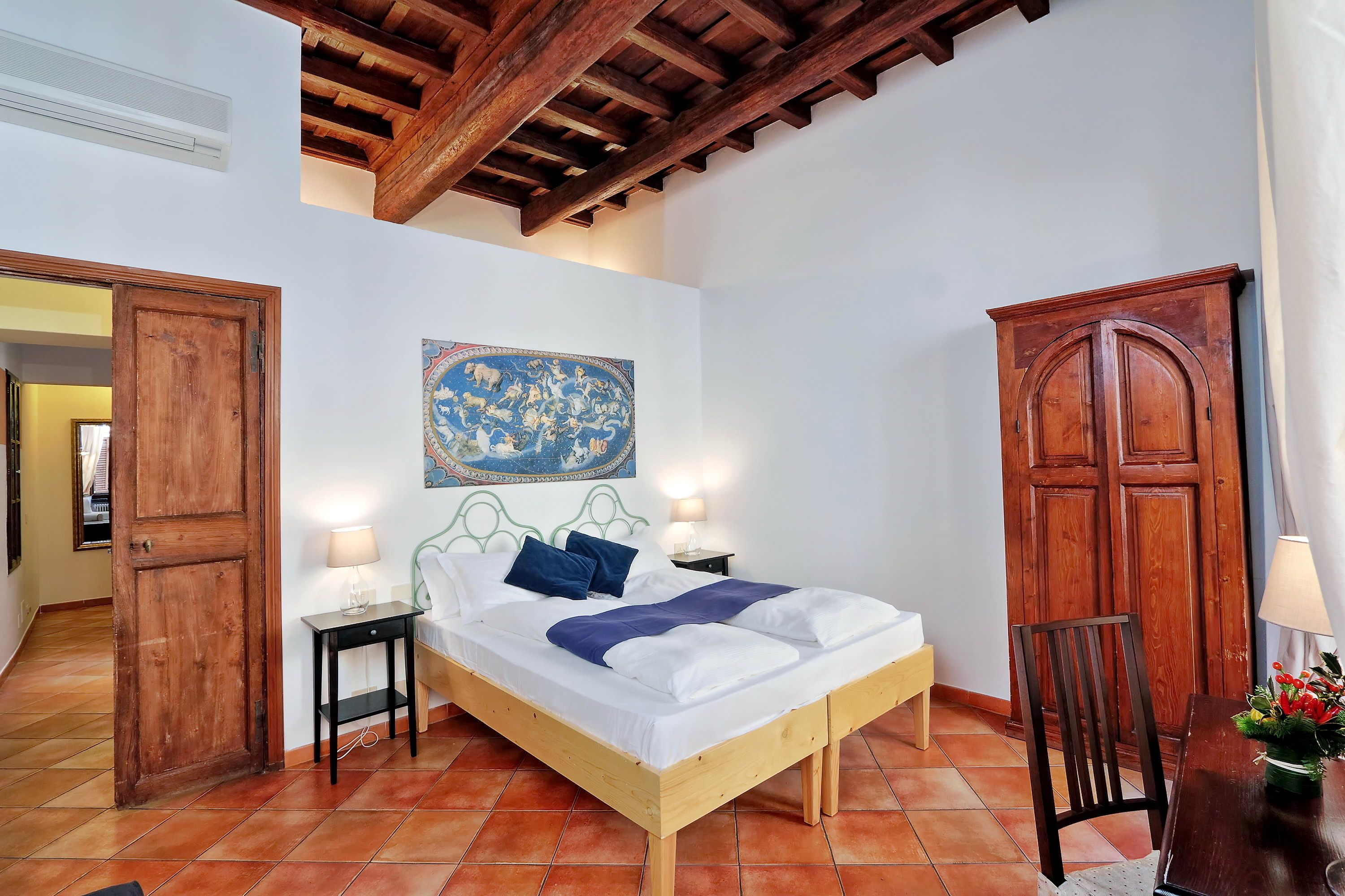 A bedroom with a wooden bed, a nightstand, a lamp, a chair, and a wooden wardrobe.