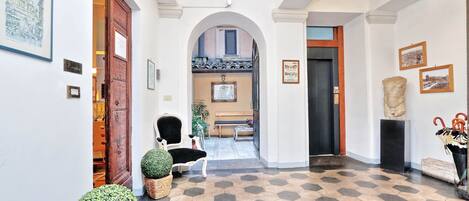 A hallway with hexagonal patterned flooring, a wooden door, a bench, and a framed picture on the wall.