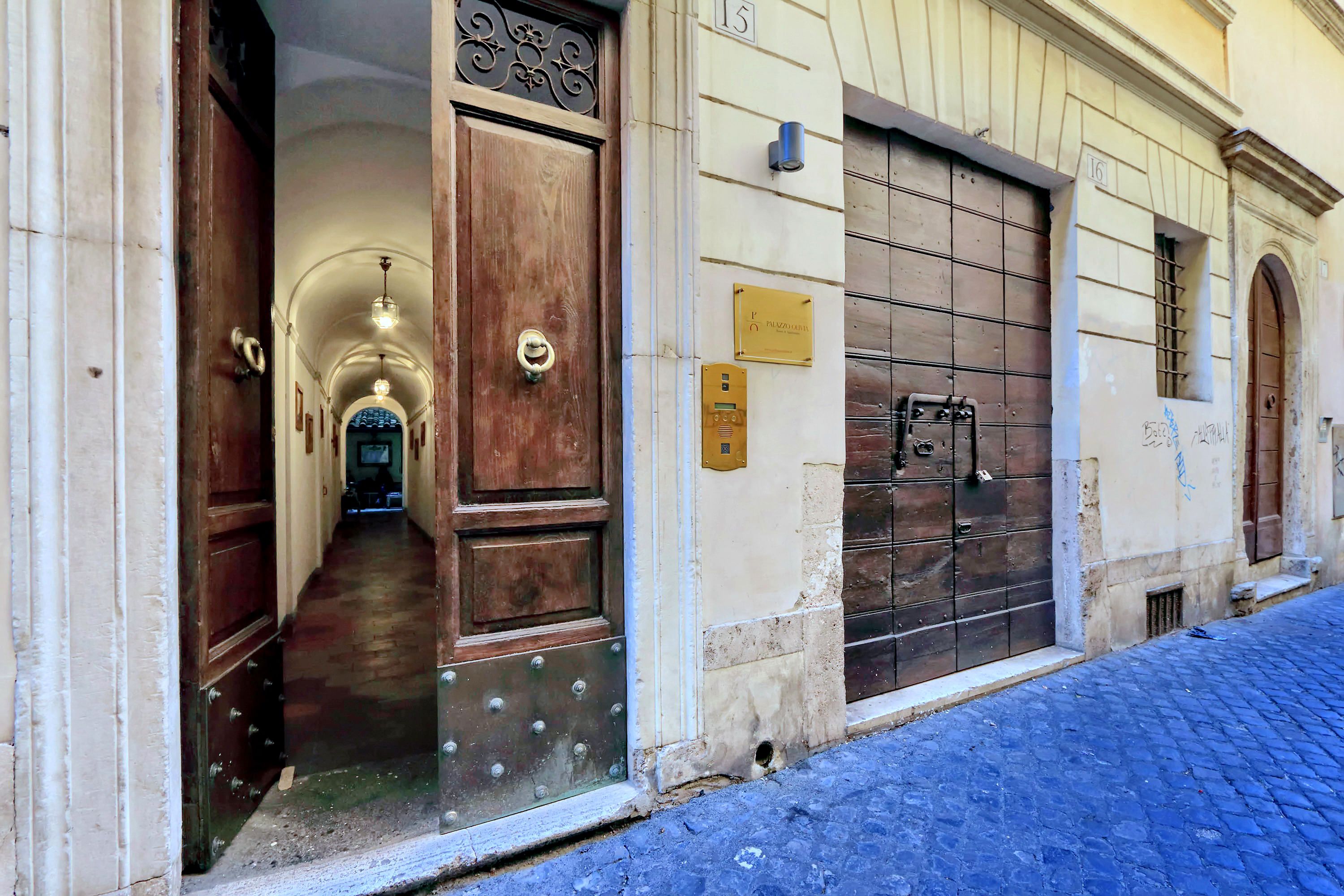 A building with a wooden door and a metal gate, a cobblestone street, and a plaque on the wall.