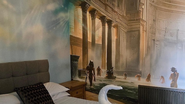 A bedroom with a large bed, a swan-shaped pillow, and a mural of classical architecture. - Stonehenge Inn (Salisbury)