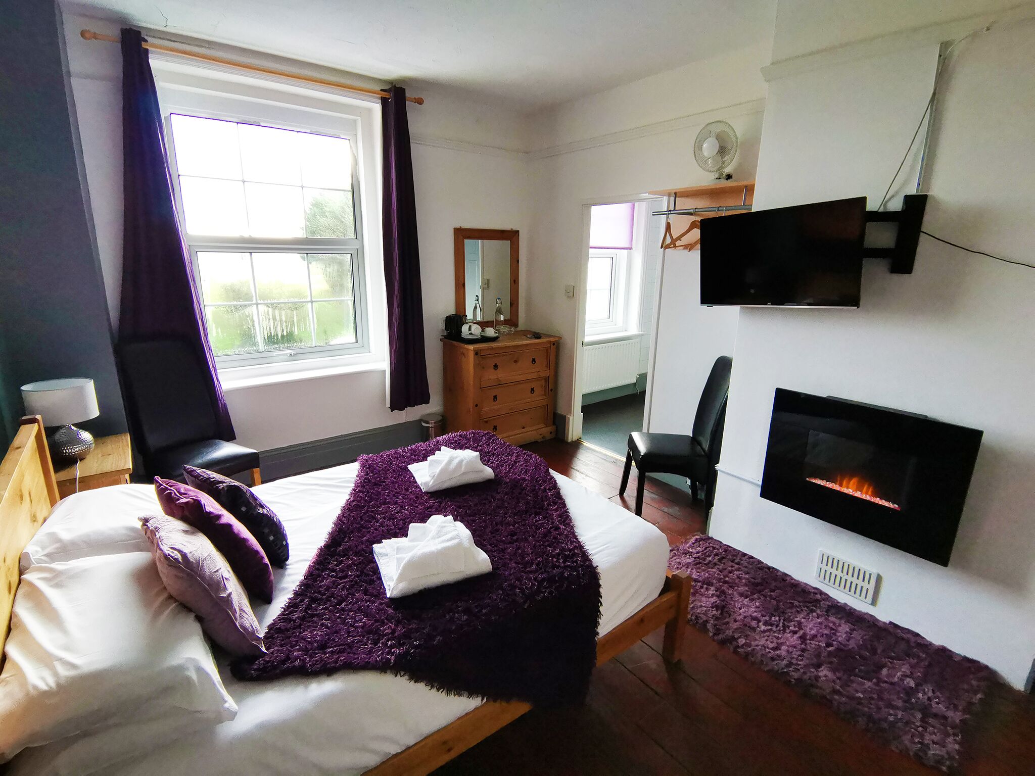A bedroom with a bed, a dresser, a chair, a TV, and a fireplace.