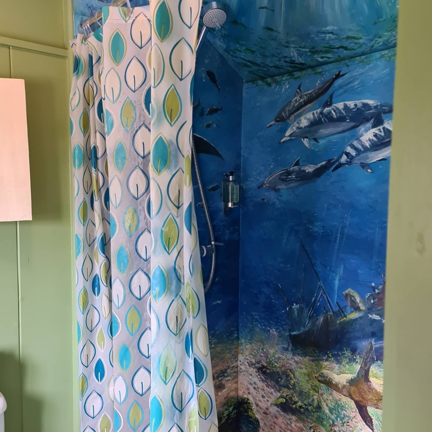 A bathroom with a shower curtain featuring a leaf pattern, a mirror, and an underwater mural of dolphins and a shipwreck.
