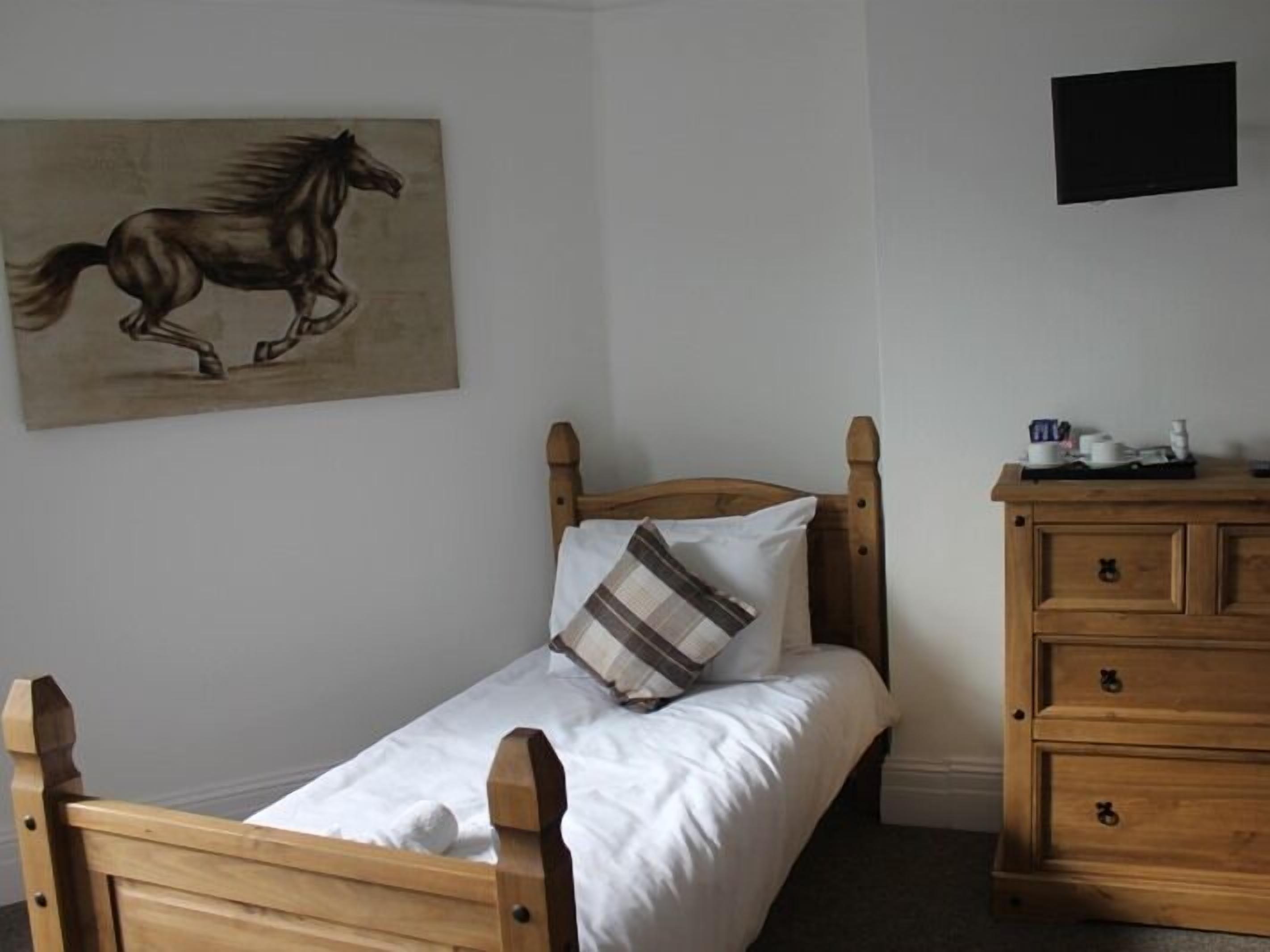 A bedroom with a wooden bed, a wooden dresser, a painting of a horse, and a flat-screen TV on the wall.