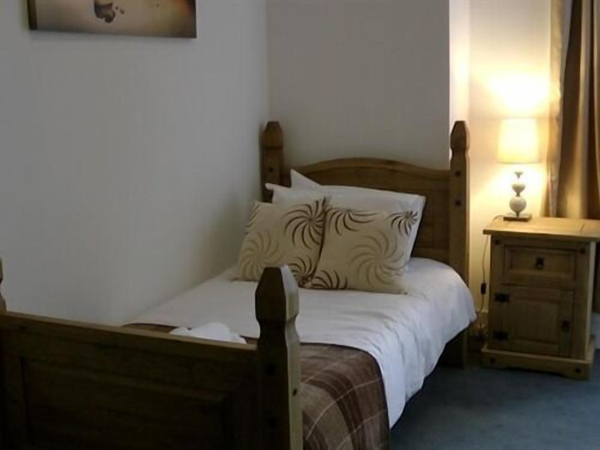 A single bed with a wooden headboard, a bedside table with a lamp, and a wall-mounted picture.