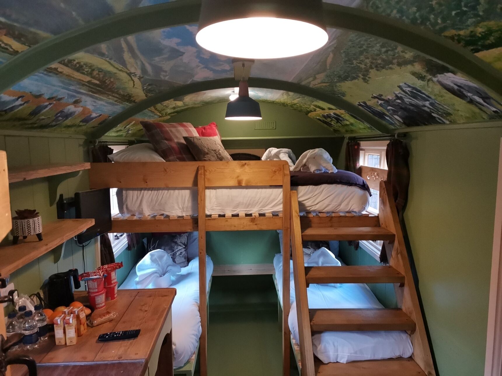 Une chambre avec un lit superposé, une échelle en bois, une table sur laquelle se trouvent divers objets, et une fresque au plafond.