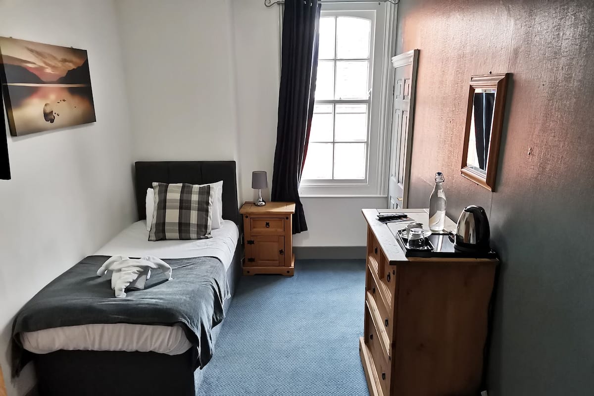 A bedroom with a bed, bedside table, dresser, and a window with curtains.