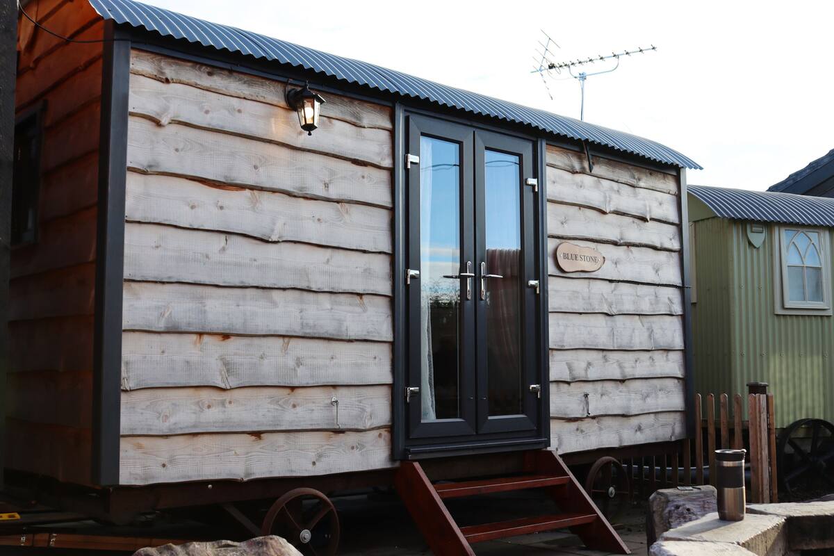 A wooden cabin with a black door and windows, a small porch, and a sign that reads "Blue Stone."