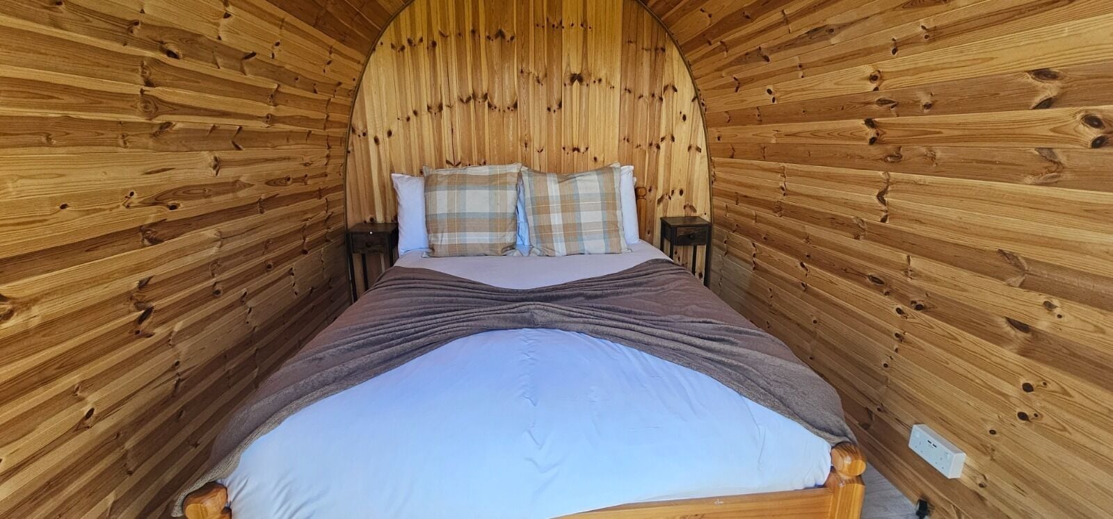 Habitación con paneles de madera, una cama, almohadas y dos mesitas de noche.