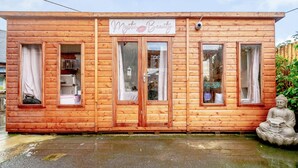 A wooden cabin with a sign reading "Mysti Beauty." It has multiple windows, a door, and a small statue of Buddha outside. - Stonehenge Inn (Salisbury)