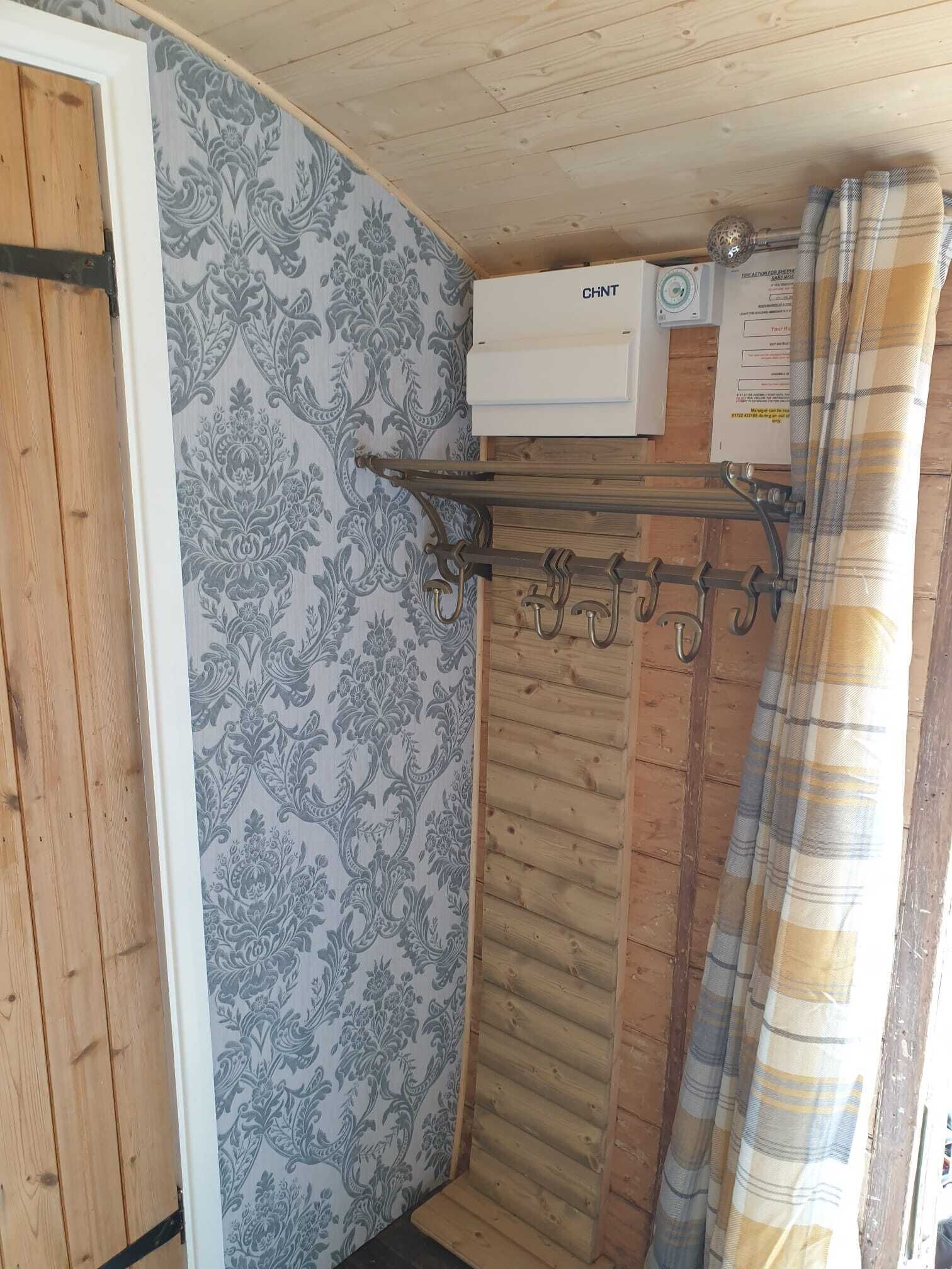 A bathroom with a wooden door, patterned wallpaper, a towel rack, a shower curtain, and a white air conditioning unit.