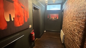 A narrow hallway with wooden flooring, a fire extinguisher, a clock, and a window with a view of a sunset. - Stonehenge Inn (Salisbury)